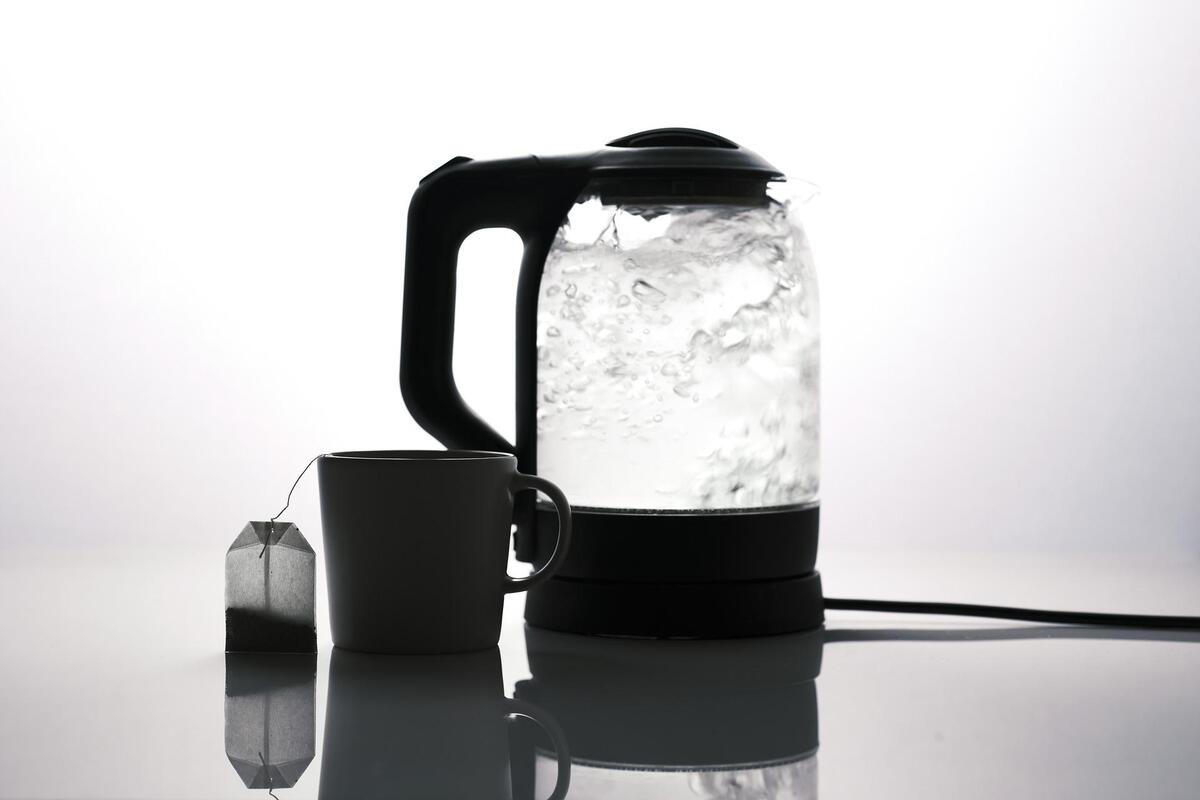 Zu sehen ist ein Wasserkocher, eine Teetasse sowie ein Teebeutel in schwarz-weiß.