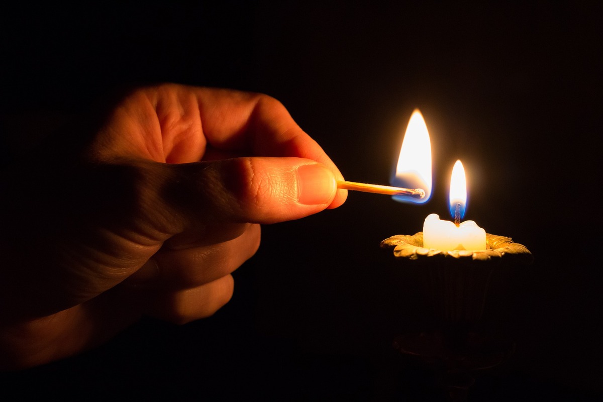 Zu sehen ist eine Hand, die mit einem Streichholz eine Kerze anzündet.